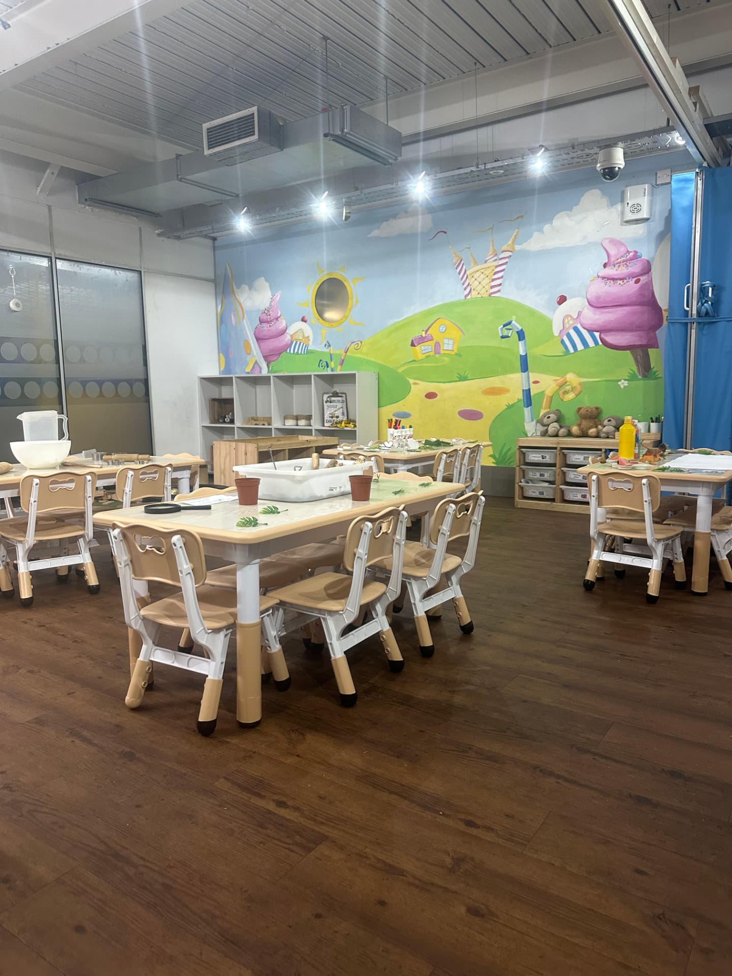 Nursery classroom with child-sized tables, chairs and an ice-cream themed mural at Teenie Weenies
