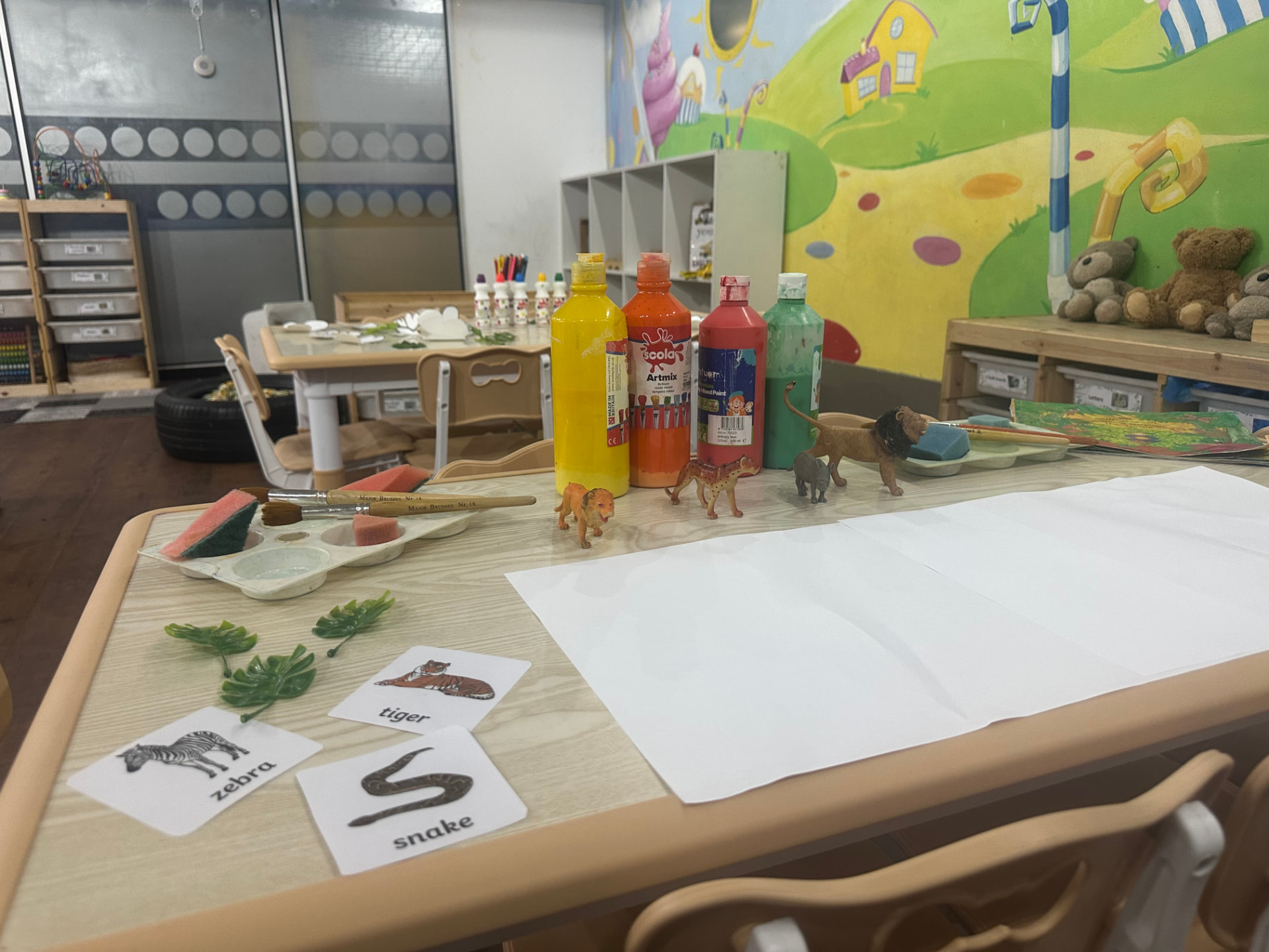 Nursery art table with paint bottles, animal figures and word flashcards